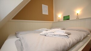 A single bed with a white mattress and pillows, a folded white towel, and two wall-mounted lamps. - Am Grünstreifen 31, Whg. 6 "Strandgut" - Apartment for 2 persons on approx. (Wyk auf Föhr)
