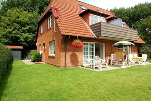A two-story house with a red-tiled roof, a covered patio with outdoor furniture, and a satellite dish. - Am Leuchtturm 7, Whg. 2 - Ferienwohnung mit 2- Zimmern auf ca. 48m² (Wyk auf Föhr)