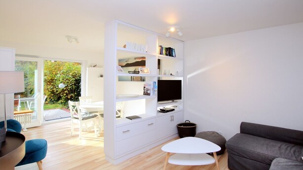 A modern living room with a white entertainment unit, a grey sofa, a small white coffee table, and a dining area with a white table and chairs. - Fasanenweg 2 b, Whg. 2 - vacation apartment in Wyk with 3 rooms, approx. 58 m² on the ground floor with (Wyk auf Föhr)
