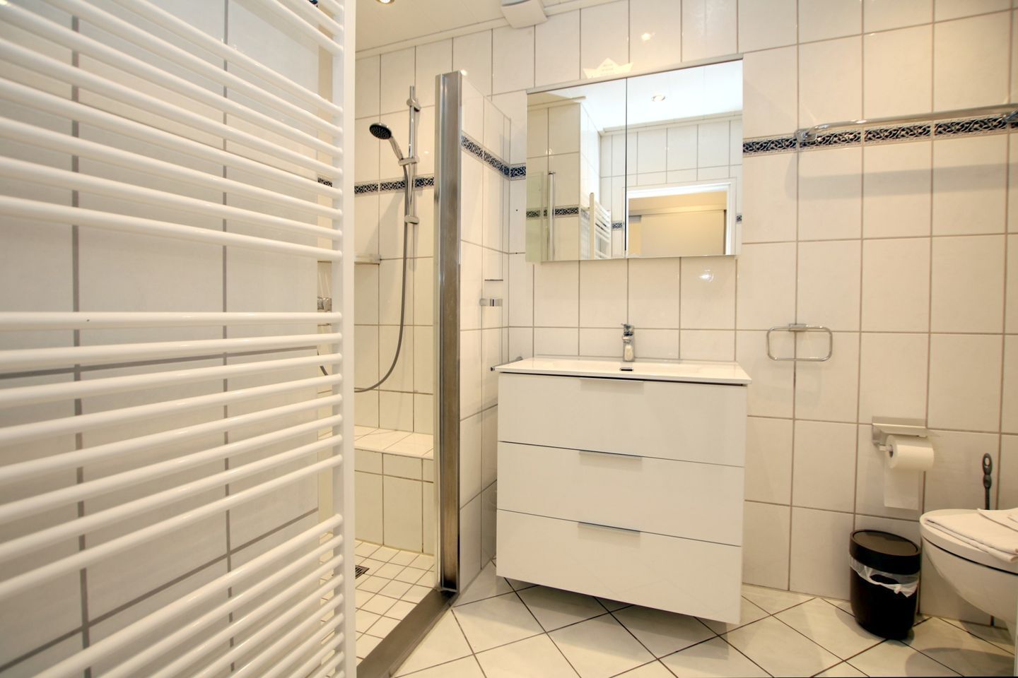 Un baño moderno con cabina de ducha de vidrio, un lavabo blanco con espejo y un inodoro.