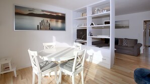 A modern living room with a dining area, white furniture, a large painting, and a bookshelf. - Fasanenweg 2 b, Whg. 2 - vacation apartment in Wyk with 3 rooms, approx. 58 m² on the ground floor with (Wyk auf Föhr)