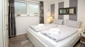 Un lit double avec des serviettes blanches soigneusement pliées, une table de chevet avec une lampe, une fenêtre avec des rideaux et un miroir fixé au mur.