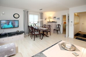 Een moderne woonkamer met een eethoek, een televisie en een keuken op de achtergrond.