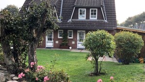 Une maison à deux étages, dotée d’un toit en pente, d’un porche à l’avant et d’une pelouse bien entretenue agrémentée de fleurs roses.