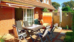 Une terrasse avec une table et des chaises, une clôture en bois et une maison en briques.