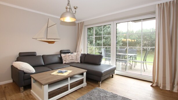 En moderne stue med en hjørnesofa, et træ sofabord og en stor skydedør, der fører ud til en udendørs terrasse.
