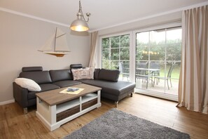 Uma sala de estar moderna com um sofá seccional, uma mesa de centro de madeira e uma grande porta de vidro deslizante que dá para um pátio externo.
