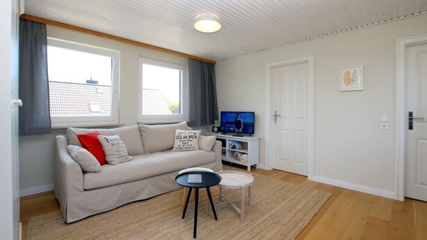 Een woonkamer met een bank, een bijzettafeltje, een televisie en een deur.