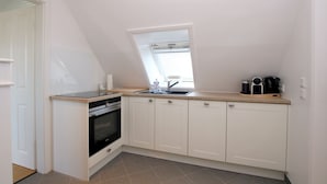 Een kleine keuken met een raam, een spoelbak, een kookplaat en kastjes.