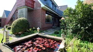 A house with a brick exterior, a red balcony, and a small pond with red lily pads. - Linge 4, Whg. 1, Hygge - vacation apartment with garden, total of 6 rooms, 4 bedrooms (Wrixum)