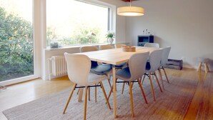 A modern dining room with a large table, six chairs, a hanging light fixture, and a view of greenery outside. - Linge 4, Whg. 1, Hygge - vacation apartment with garden, total of 6 rooms, 4 bedrooms (Wrixum)