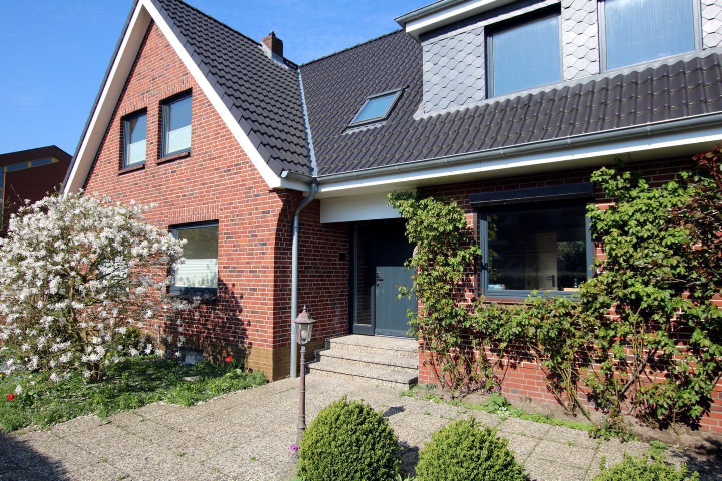 Ein zweistöckiges Haus mit Ziegelaußenwand, dunklem Dach und einer Haustür mit Stufen.