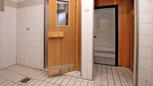 Een badkamer met een houten deur, een douchegedeelte en betegelde vloer.