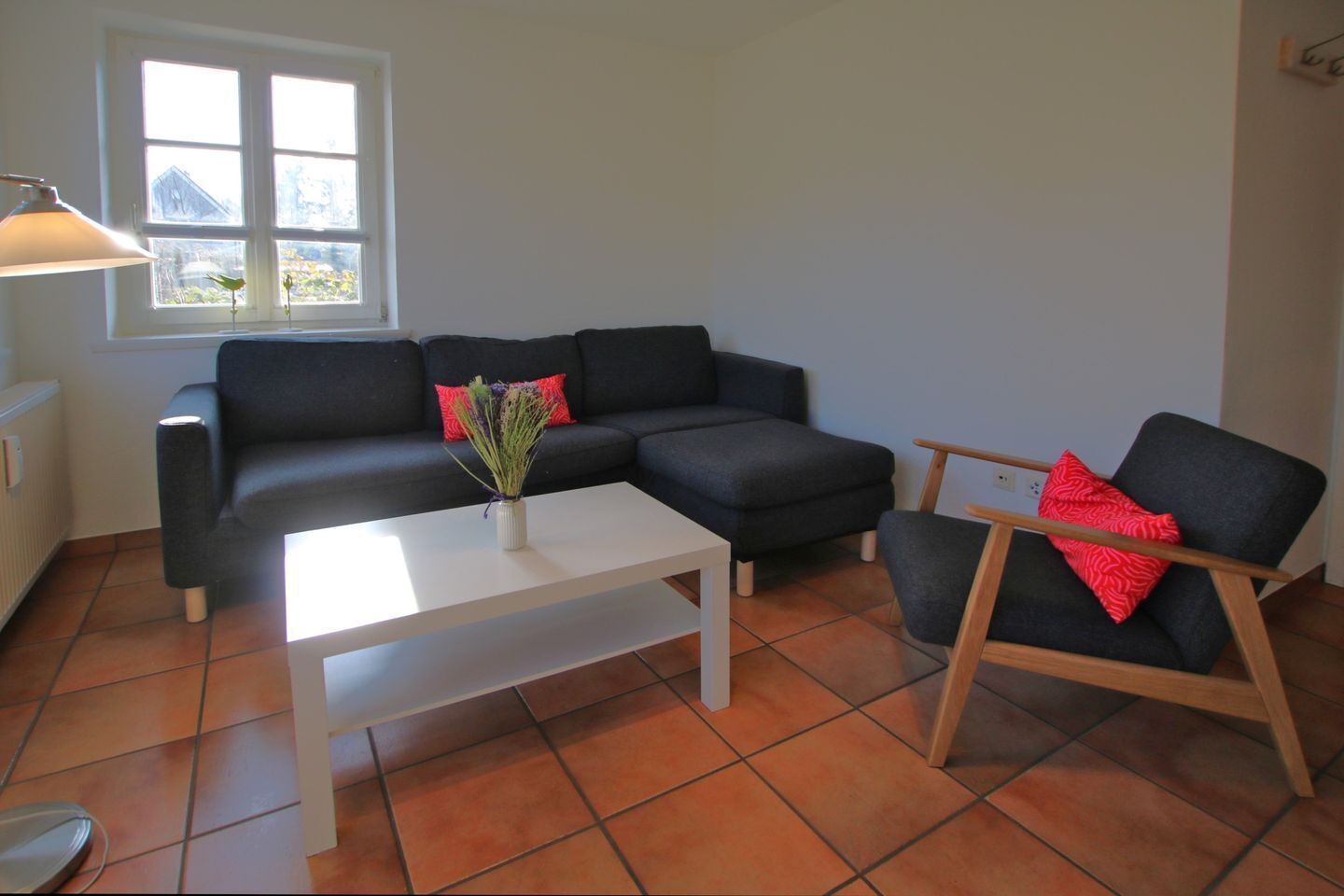 A living room with a black sofa, a wooden chair, a white coffee table, and a window with a view of greenery.
