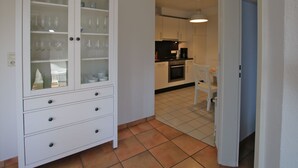 Een kleine keuken met witte kastjes, een zwart aanrecht en een witte stoel.