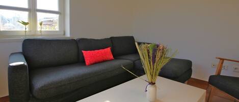 A modern living room with a dark grey sofa, a red pillow, and a white coffee table.