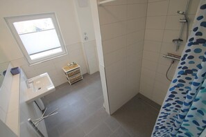 Een kleine badkamer met een raam, wastafel en douche.