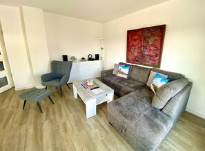 Un salon moderne avec un canapé gris, un fauteuil bleu, une petite table basse et un meuble blanc.