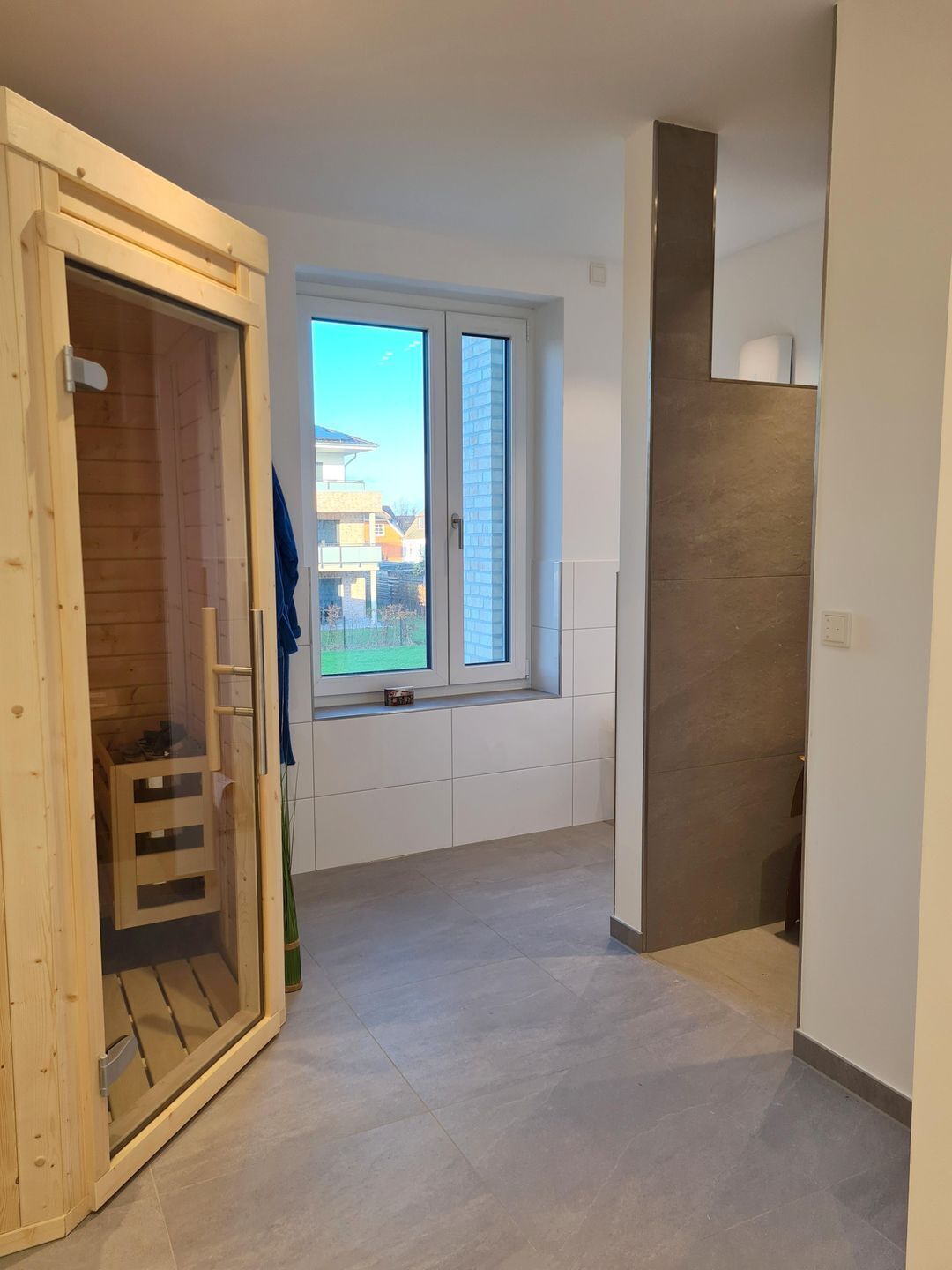 A modern interior with a wooden sliding door leading to a balcony, a large window with a view of buildings, and a tiled floor.