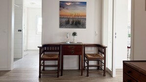A room with a desk and two chairs, a painting on the wall, and a view of a beach at sunset. - 2107 - with sea view Strandwiese - 2107 - Penthouse Strandwiese 9 - Apartment 7 (Dahme)