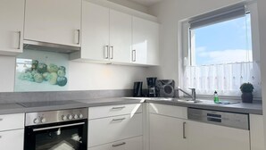A modern kitchen with white cabinets, a built-in oven, a dishwasher, and a window with a view. - 2107 - with sea view Strandwiese - 2107 - Penthouse Strandwiese 9 - Apartment 7 (Dahme)