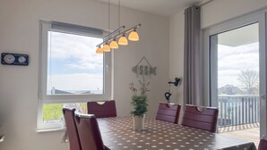 A dining area with a table covered in a star-patterned tablecloth, surrounded by chairs, a potted plant, and a wall-mounted clock. - 2107 - with sea view Strandwiese - 2107 - Penthouse Strandwiese 9 - Apartment 7 (Dahme)