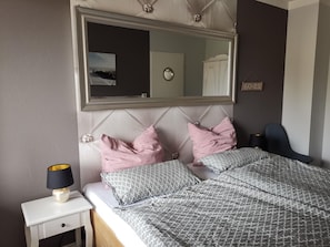 Quarto com cama, mesa de cabeceira, abajur e espelho.