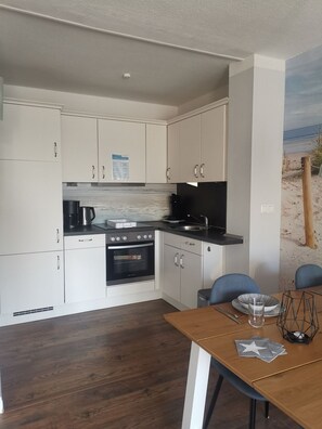 Una cucina compatta con mobili bianchi, un piano cottura nero e un'area pranzo con tavolo in legno e sedie blu.