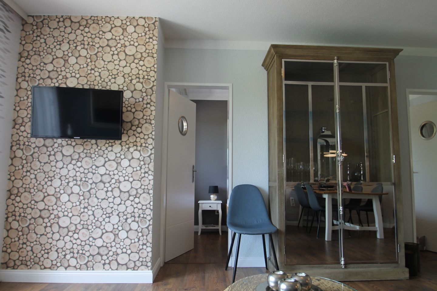 A living room with a stone wall, a flat-screen TV, a dining area with a glass door, and a small side table.