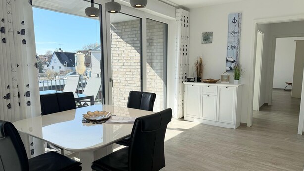 A modern dining area with a white table, black chairs, and pendant lighting. - 2605 - Strandwiese 18 - Apartment 2605 in the Strandwiese (Dahme)