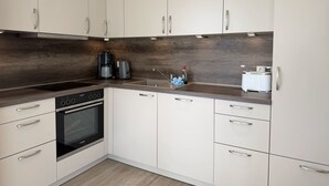 A modern kitchen with white cabinets, a built-in oven, a coffee maker, and a toaster. - 2605 - Strandwiese 18 - Apartment 2605 in the Strandwiese (Dahme)
