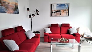 A modern living room with two red sofas, a glass coffee table, and artwork on the walls. - 2605 - Strandwiese 18 - Apartment 2605 in the Strandwiese (Dahme)