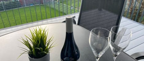 A balcony with a table, a bottle of wine, two glasses, and a potted plant.