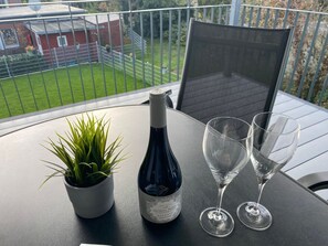 Ein Balkon mit Tisch, einer Weinflasche, zwei Gläsern und einem Blumentopf.