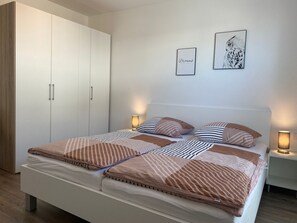 A bedroom with a bed, two bedside tables, a wardrobe, and two wall-mounted pictures. - 2606 - Strandwiese 18 - Apartment 2606 in the Strandwiese Dahme (Dahme)