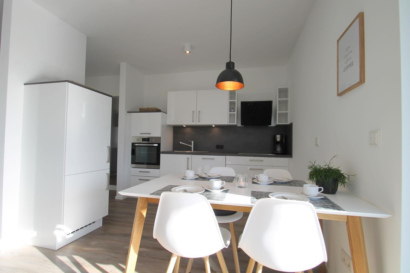 Une cuisine moderne avec des meubles blancs, un plan de travail noir et un coin repas comprenant une table et des chaises blanches.