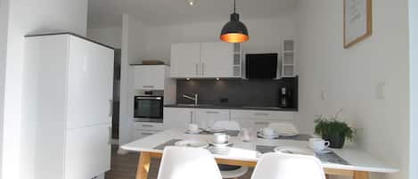 A modern kitchen with white cabinets, a black countertop, and a dining area with a white table and chairs.