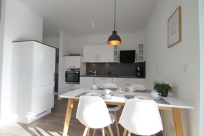 Une cuisine moderne avec des meubles blancs, un plan de travail noir et un coin repas comprenant une table et des chaises blanches.