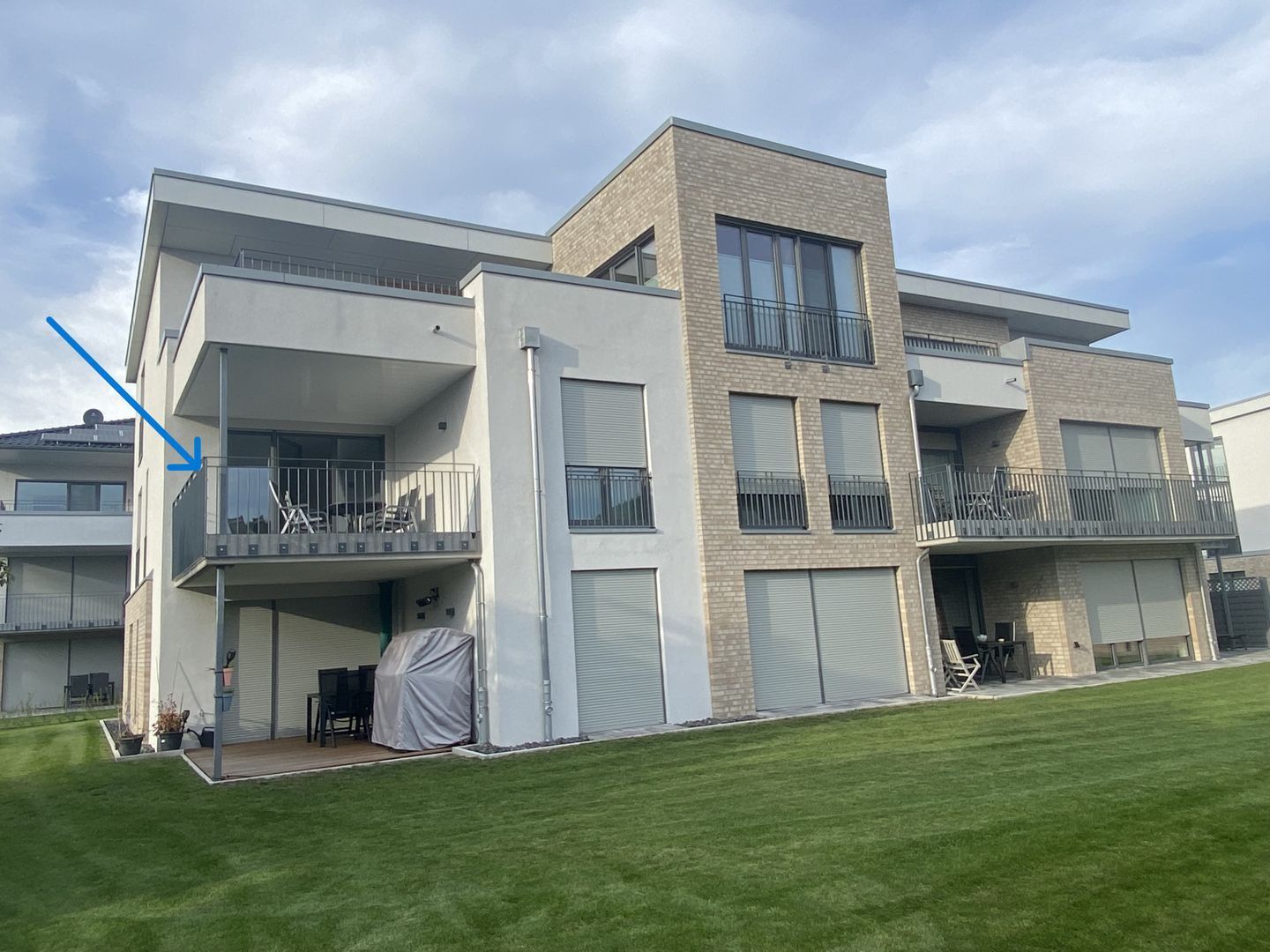 Un edificio residencial moderno de varios pisos con balcones, ventanas amplias y una zona de estar al aire libre cubierta.