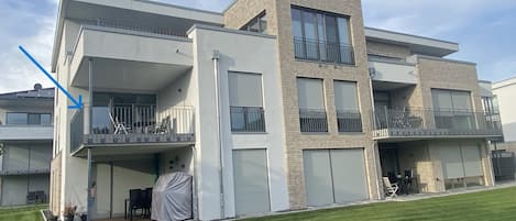 Un edificio residencial moderno de varios pisos con balcones, ventanas amplias y una zona de estar al aire libre cubierta.