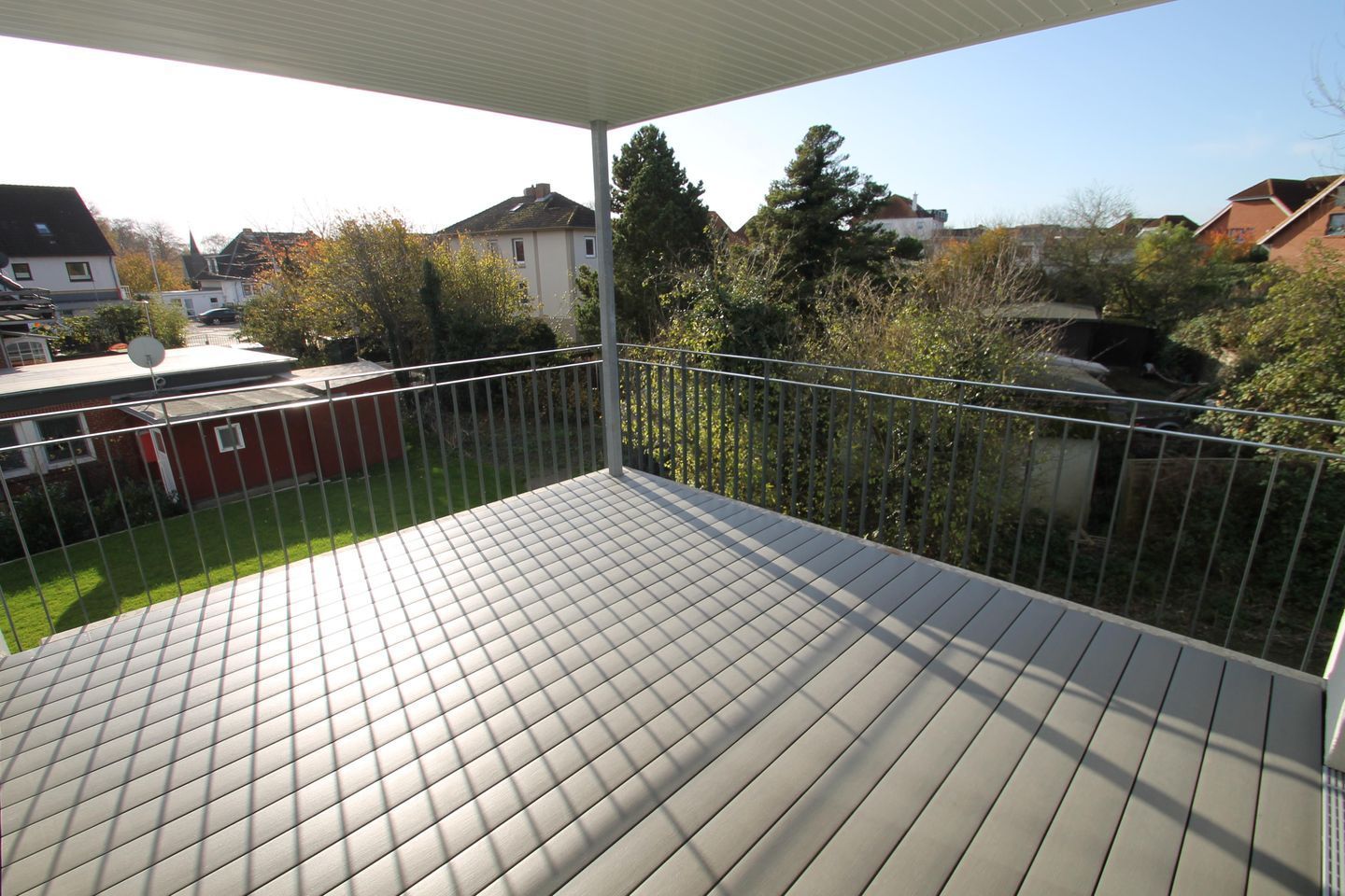 Un balcon doté d’un sol carrelé, d’une rambarde en métal et offrant une vue sur des maisons et des arbres.