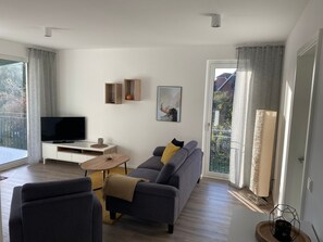 Ein modernes Wohnzimmer mit einer Couch, einem Couchtisch, einem Fernseher und einem Balkon mit Vorhängen.