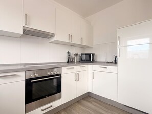 A modern kitchen with white cabinetry, a stainless steel oven, a microwave, and a refrigerator. - 2106 - Strandwiese - 2106 - Strandwiese 9 - Apartment 6 (Dahme)