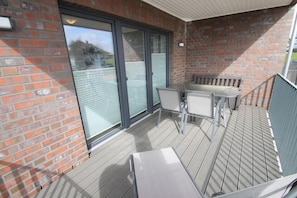 A covered outdoor area with a brick wall, sliding glass doors, and a seating area with a table and chairs.