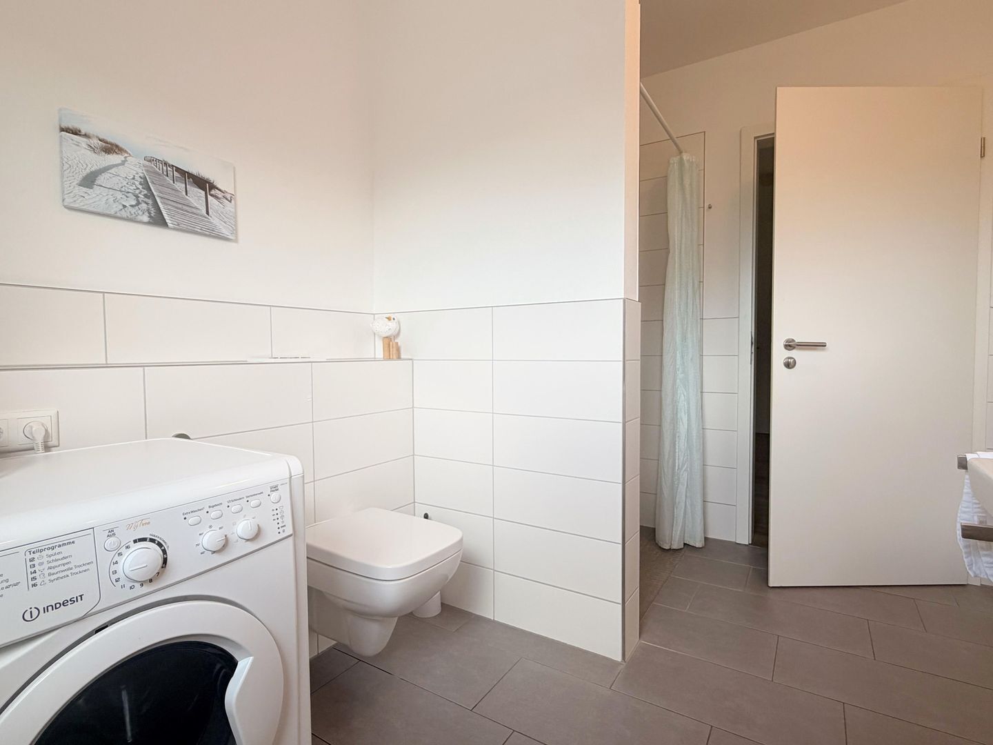 A modern bathroom with a washing machine, toilet, and a shower area.