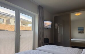 Une chambre d’hôtel avec un lit, un téléviseur fixé au mur, une fenêtre et une porte donnant sur une autre pièce.