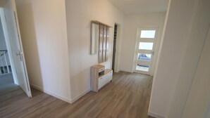 Un pasillo con suelo de madera, una puerta blanca con ventana y un pequeño armario blanco.