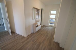 A hallway with wooden flooring, a white door with a window, and a small white cabinet. - 2106 - Strandwiese - 2106 - Strandwiese 9 - Apartment 6 (Dahme)