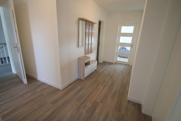 A hallway with wooden flooring, a white door with a window, and a small white cabinet.
