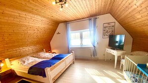 Un dormitorio acogedor en el ático con techo de madera, una cama, un escritorio con televisor y una cuna.